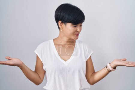 Photo for Young asian woman with short hair standing over isolated background smiling showing both hands open palms, presenting and advertising comparison and balance - Royalty Free Image