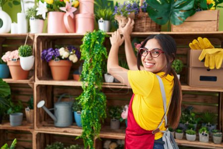 Téléchargez les photos : Young beautiful arab woman florist smiling confident holding plant of shelving at flower shop - en image libre de droit
