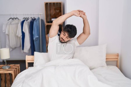Téléchargez les photos : Young hispanic man waking up stretching arms at bedroom - en image libre de droit