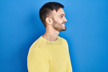 Téléchargez les photos : Homme hispanique debout sur fond bleu regardant vers le côté, pose de profil relax avec visage naturel et sourire confiant. - en image libre de droit