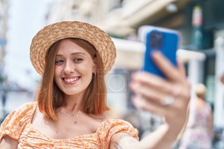 Téléchargez les photos : Jeune rousse femme touriste portant chapeau d'été faire selfie par smartphone à la rue - en image libre de droit