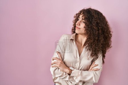 Téléchargez les photos : Femme hispanique avec les cheveux bouclés debout sur fond rose regardant sur le côté avec les bras croisés convaincu et confiant - en image libre de droit