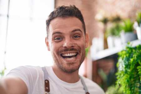 Téléchargez les photos : Jeune homme hispanique fleuriste souriant confiant faire selfie par caméra chez le fleuriste - en image libre de droit