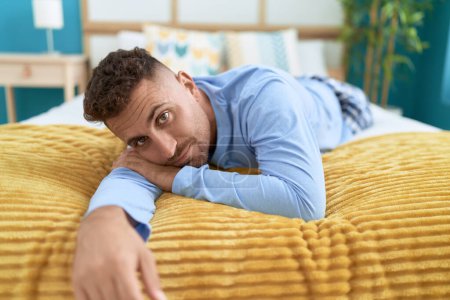 Téléchargez les photos : Jeune homme hispanique couché sur le lit avec une expression détendue dans la chambre - en image libre de droit