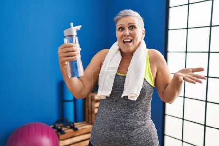 Photo for Middle age woman wearing sportswear and towel holding water celebrating achievement with happy smile and winner expression with raised hand - Royalty Free Image