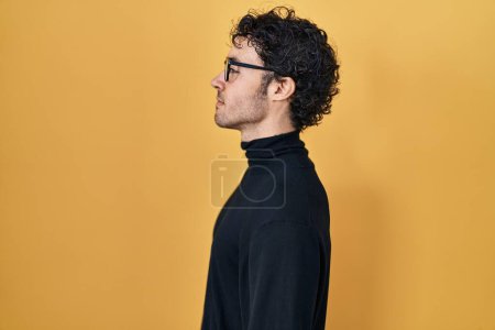 Photo for Hispanic man standing over yellow background looking to side, relax profile pose with natural face and confident smile. - Royalty Free Image
