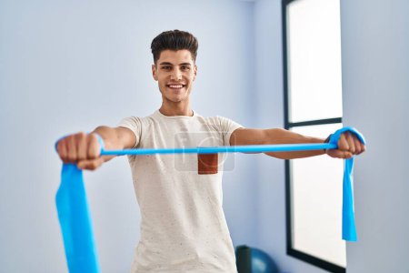 Photo for Young hispanic man smiling confident training using elastic band at sport center - Royalty Free Image