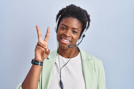 Téléchargez les photos : Femme afro-américaine portant un casque d'agent du centre d'appel souriant regardant la caméra montrant des doigts faisant signe de victoire. numéro deux. - en image libre de droit