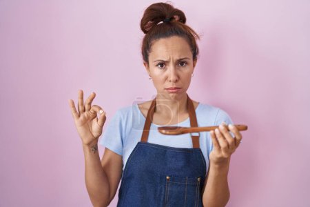 Foto de Brunette woman wearing professional cook apron holding wooden spoon depressed and worry for distress, crying angry and afraid. sad expression. - Imagen libre de derechos