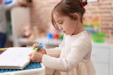 Téléchargez les photos : Adorable fille coupant du papier debout à la maternelle - en image libre de droit