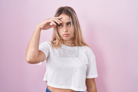Photo for Young blonde woman standing over pink background worried and stressed about a problem with hand on forehead, nervous and anxious for crisis - Royalty Free Image
