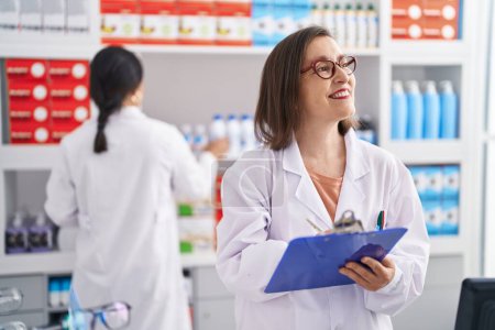 Photo for Two women pharmacist smiling confident writing on document at pharmacy - Royalty Free Image