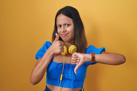 Photo for Hispanic young woman standing over yellow background doing thumbs up and down, disagreement and agreement expression. crazy conflict - Royalty Free Image