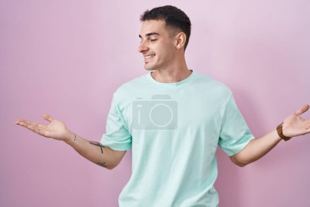 Photo for Handsome hispanic man standing over pink background smiling showing both hands open palms, presenting and advertising comparison and balance - Royalty Free Image