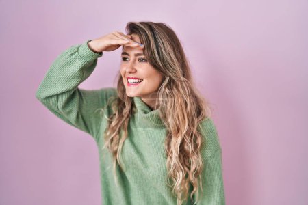 Photo for Young caucasian woman standing over pink background very happy and smiling looking far away with hand over head. searching concept. - Royalty Free Image
