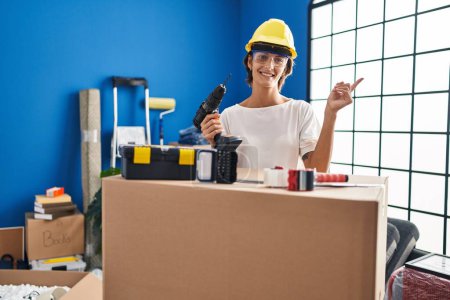 Photo for Brunette woman holding screwdriver at new home smiling happy pointing with hand and finger to the side - Royalty Free Image