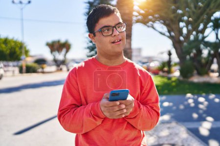 Téléchargez les photos : Homme trisomique souriant confiant en utilisant smartphone au parc - en image libre de droit