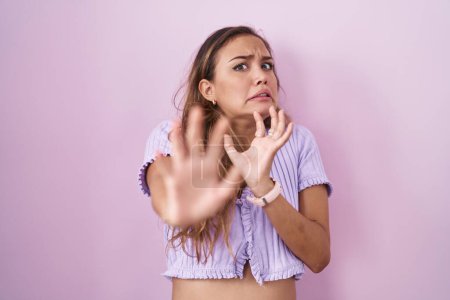Photo for Young hispanic woman standing over pink background afraid and terrified with fear expression stop gesture with hands, shouting in shock. panic concept. - Royalty Free Image