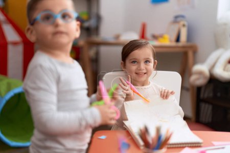 Foto de Adorable girl and boy sitting on table cutting paper at kindergarten - Imagen libre de derechos