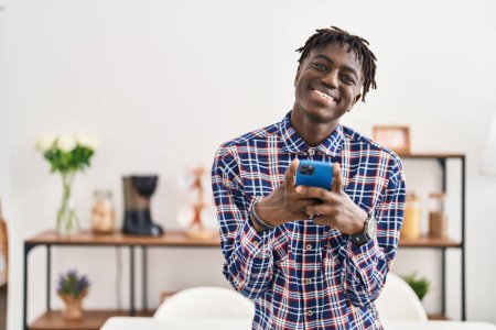 Foto de African american man using smartphone standing at home - Imagen libre de derechos