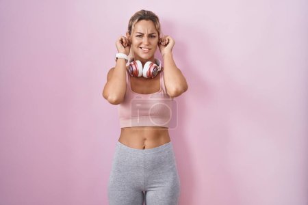 Téléchargez les photos : Young blonde woman wearing sportswear and headphones covering ears with fingers with annoyed expression for the noise of loud music. deaf concept. - en image libre de droit