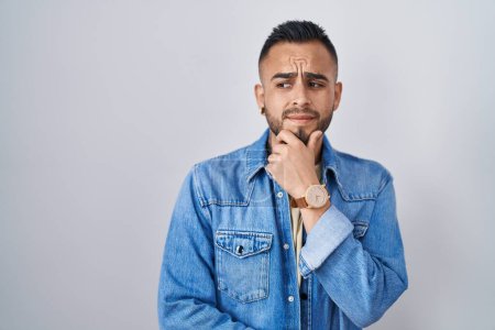 Photo for Young hispanic man standing over isolated background thinking worried about a question, concerned and nervous with hand on chin - Royalty Free Image