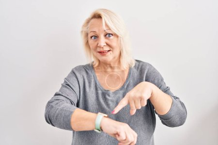 Téléchargez les photos : Middle age caucasian woman standing over white background in hurry pointing to watch time, impatience, upset and angry for deadline delay - en image libre de droit