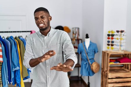 Foto de Joven hombre afroamericano que trabaja como gerente en boutique minorista expresión disgustada, disgustado y temeroso haciendo cara de asco porque la reacción de aversión. con las manos levantadas - Imagen libre de derechos