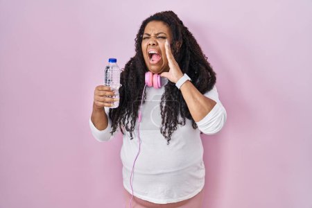 Téléchargez les photos : Plus size hispanic woman wearing sportswear and headphones shouting and screaming loud to side with hand on mouth. communication concept. - en image libre de droit