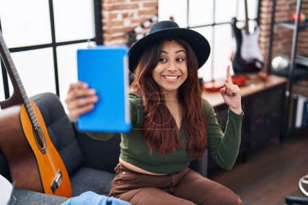 Foto de Hispanic young woman doing video call with tablet smiling with an idea or question pointing finger with happy face, number one - Imagen libre de derechos