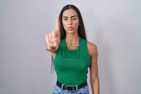Foto de Mujer joven de pie sobre un fondo aislado señalando con el dedo hacia arriba y la expresión enojada, sin mostrar ningún gesto - Imagen libre de derechos