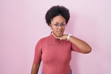 Téléchargez les photos : Beautiful african woman with curly hair standing over pink background cutting throat with hand as knife, threaten aggression with furious violence - en image libre de droit