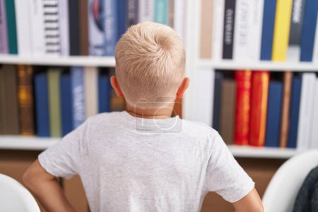 Photo for Adorable toddler looking for book of shelving at classroom - Royalty Free Image
