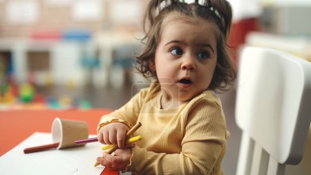 Foto de Adorable estudiante hispana sentada en la mesa dibujando sobre papel en el jardín de infantes - Imagen libre de derechos