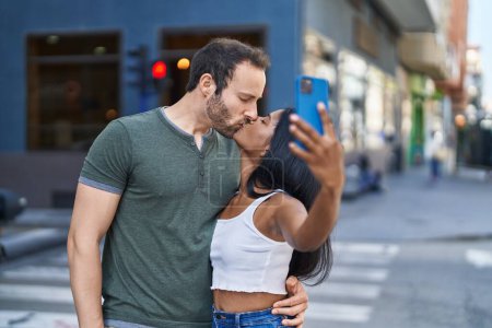 Foto de Hombre y mujer interracial pareja haciendo selfie por teléfono inteligente besos en la calle - Imagen libre de derechos
