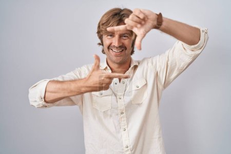 Foto de Middle age man standing over isolated background smiling making frame with hands and fingers with happy face. creativity and photography concept. - Imagen libre de derechos