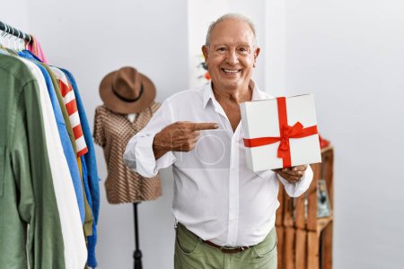 Téléchargez les photos : Senior homme tenant cadeau au magasin de détail souriant heureux pointant avec la main et le doigt - en image libre de droit