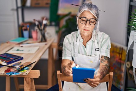 Foto de Mujer artista de pelo gris de mediana edad usando touchpad en el estudio de arte - Imagen libre de derechos