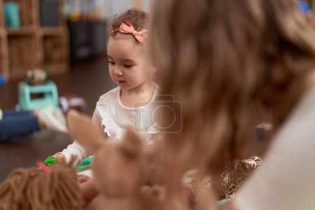 Foto de Adorable chica caucásica jugando con muñecas sentadas en el suelo en el jardín de infantes - Imagen libre de derechos