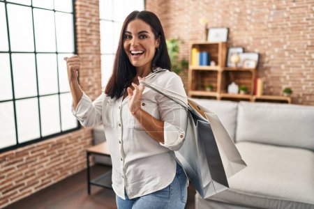 Téléchargez les photos : Jeune femme hispanique tenant des sacs à provisions pointant le pouce vers le côté souriant heureux avec la bouche ouverte - en image libre de droit