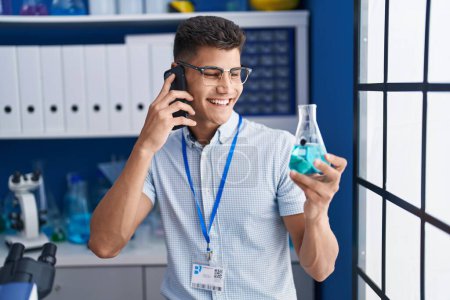 Téléchargez les photos : Young hispanic man scientist talking on the smartphone holding test tube at laboratory - en image libre de droit