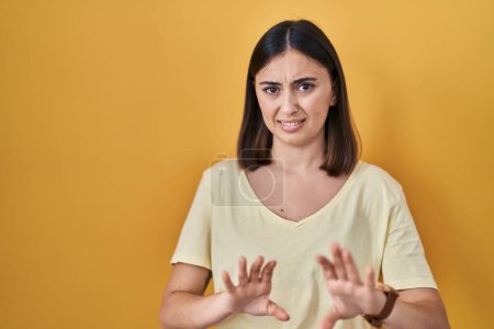 Téléchargez les photos : Hispanic girl wearing casual t shirt over yellow background disgusted expression, displeased and fearful doing disgust face because aversion reaction. - en image libre de droit