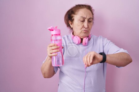 Foto de Mujer mayor que usa ropa deportiva y auriculares que comprueban la hora en el reloj de pulsera, relajado y seguro - Imagen libre de derechos