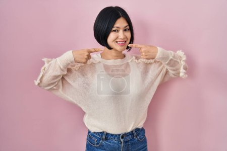 Photo for Young asian woman standing over pink background smiling cheerful showing and pointing with fingers teeth and mouth. dental health concept. - Royalty Free Image