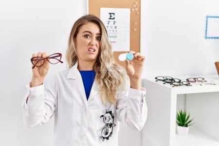 Photo for Young beautiful optician woman holding glasses and contact lenses clueless and confused expression. doubt concept. - Royalty Free Image