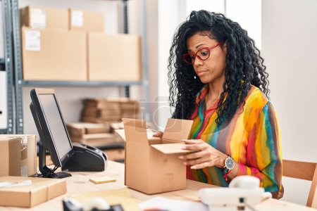 Photo for Middle age hispanic woman working at small business ecommerce looking inside box skeptic and nervous, frowning upset because of problem. negative person. - Royalty Free Image