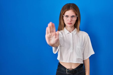 Photo for Beautiful woman standing over blue background doing stop sing with palm of the hand. warning expression with negative and serious gesture on the face. - Royalty Free Image