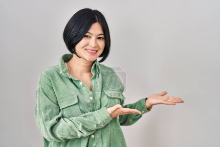 Foto de Young asian woman standing over white background inviting to enter smiling natural with open hand - Imagen libre de derechos