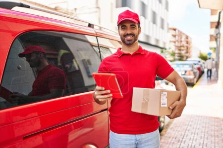 Photo for Young hispanic man courier using touchpad holding package at street - Royalty Free Image