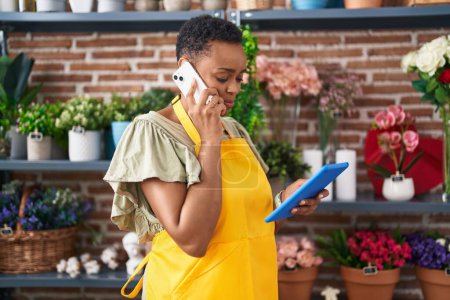 Téléchargez les photos : Afro-américaine femme fleuriste parler sur smartphone en utilisant touchpad chez le fleuriste - en image libre de droit